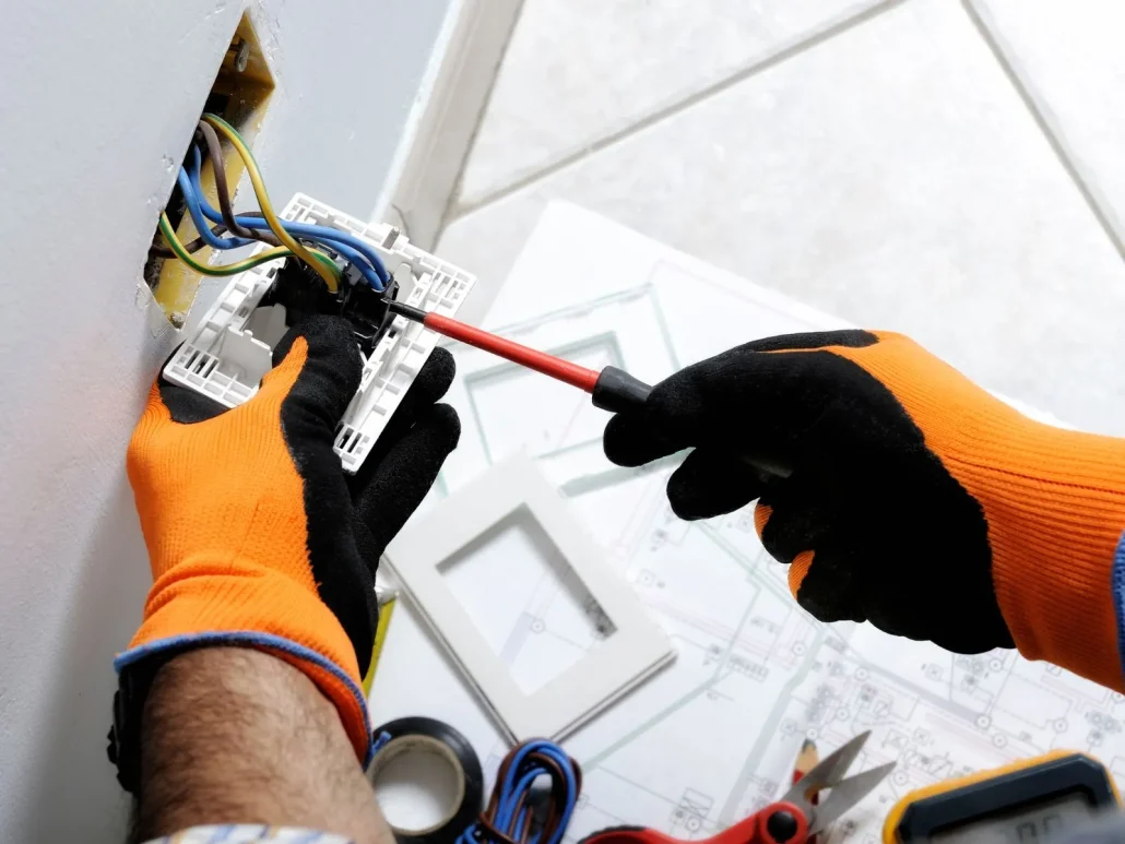 mani di elettricista con guanti che lavorano su presa di corrente